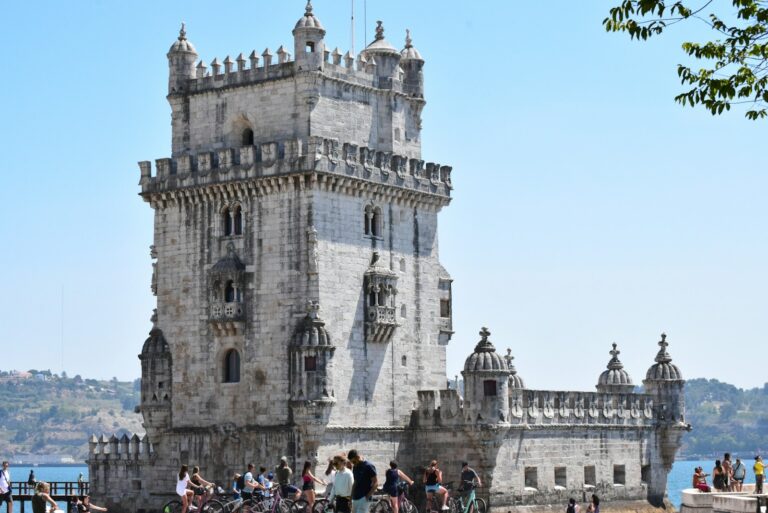 a large stone building with people walking around with Belém Tower in the background